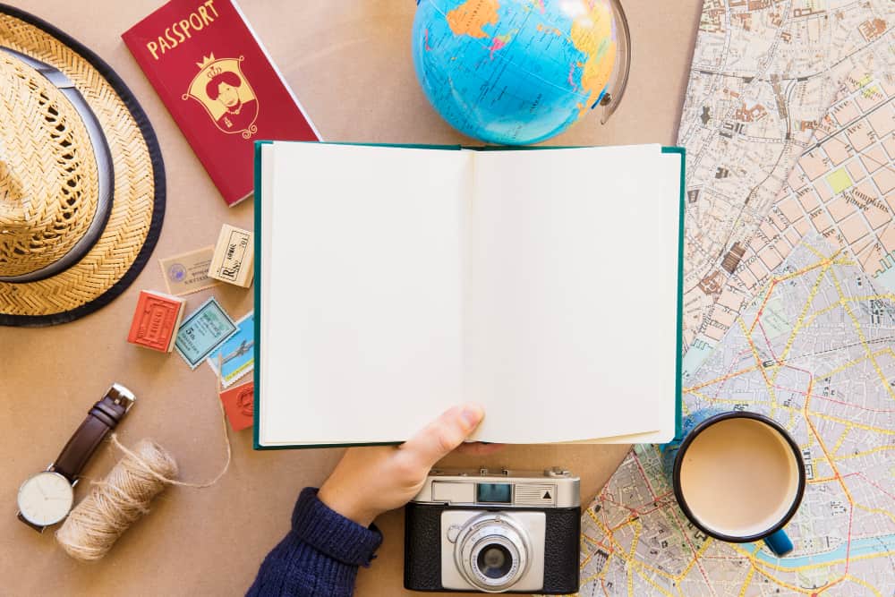 Préparation de voyage avec carnet vierge, passeport rouge, globe terrestre, carte touristique et chapeau de paille - idéal pour planifier et optimiser son cashback en voyage